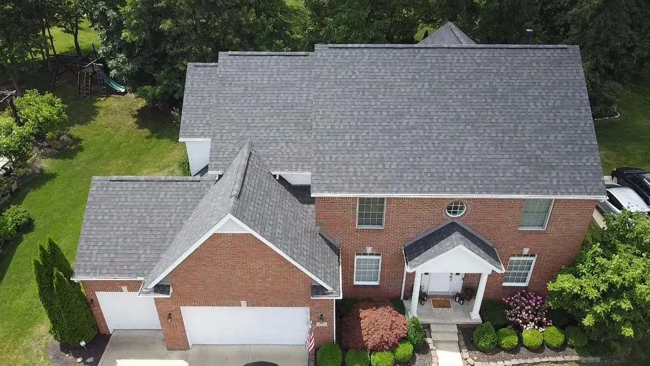 Drone view of a brick two-story colonial with a new gray architectural shingle roof and attached garage