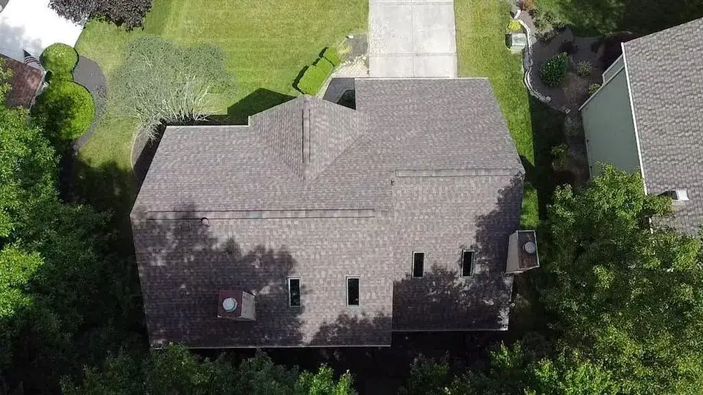 Top-down drone view of a brown architectural shingle roof on a house surrounded by mature trees
