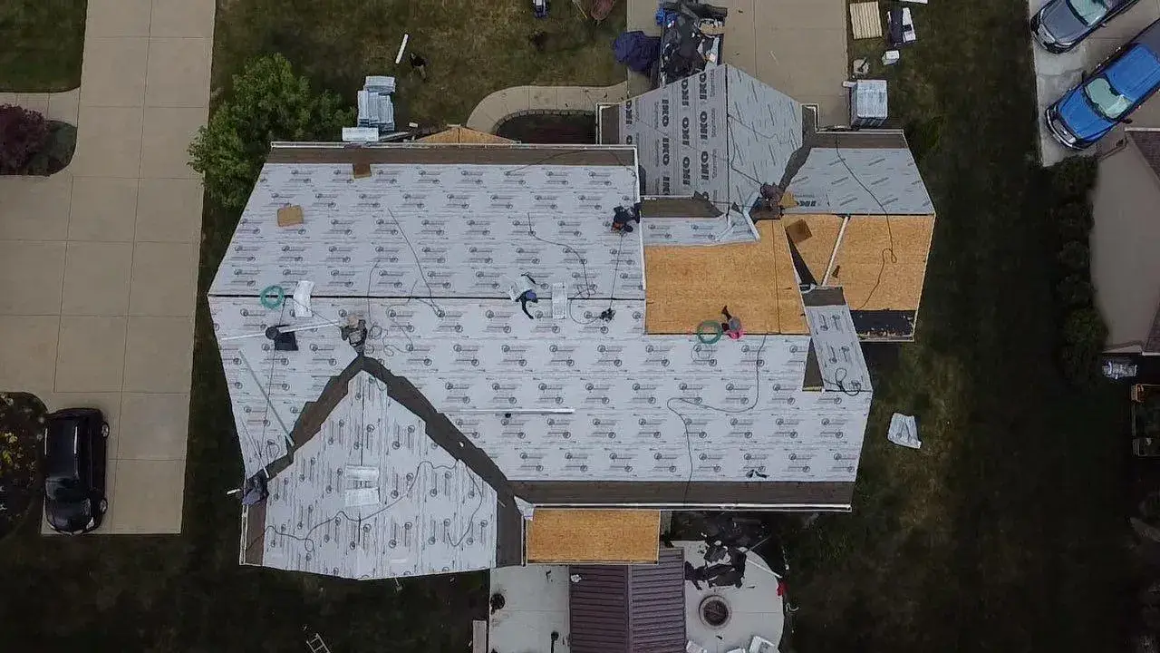 Roof replacement in progress from above: old shingles stripped, new decking patched in and synthetic underlayment going down