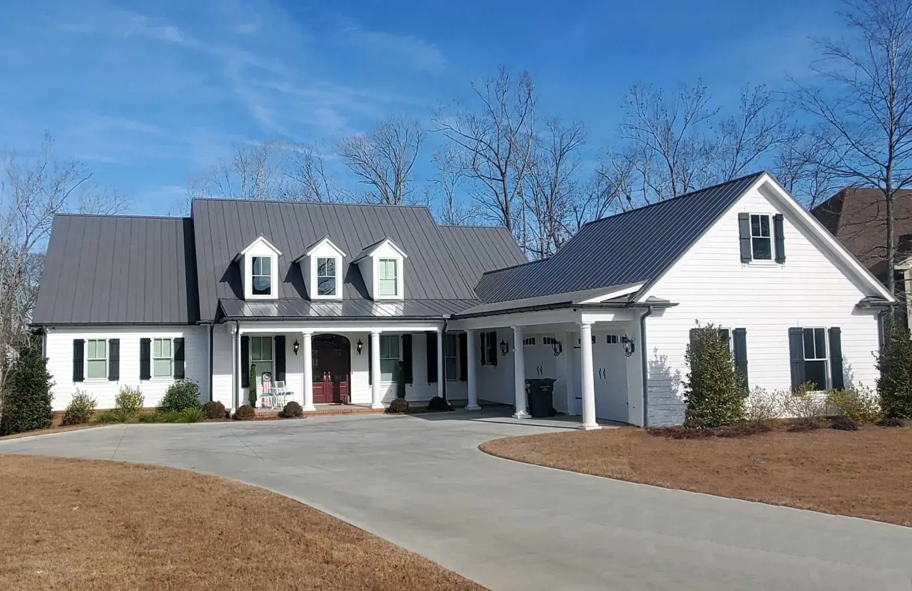 White farmhouse-style home with a charcoal 5V crimp metal roof, three dormers and a covered porch